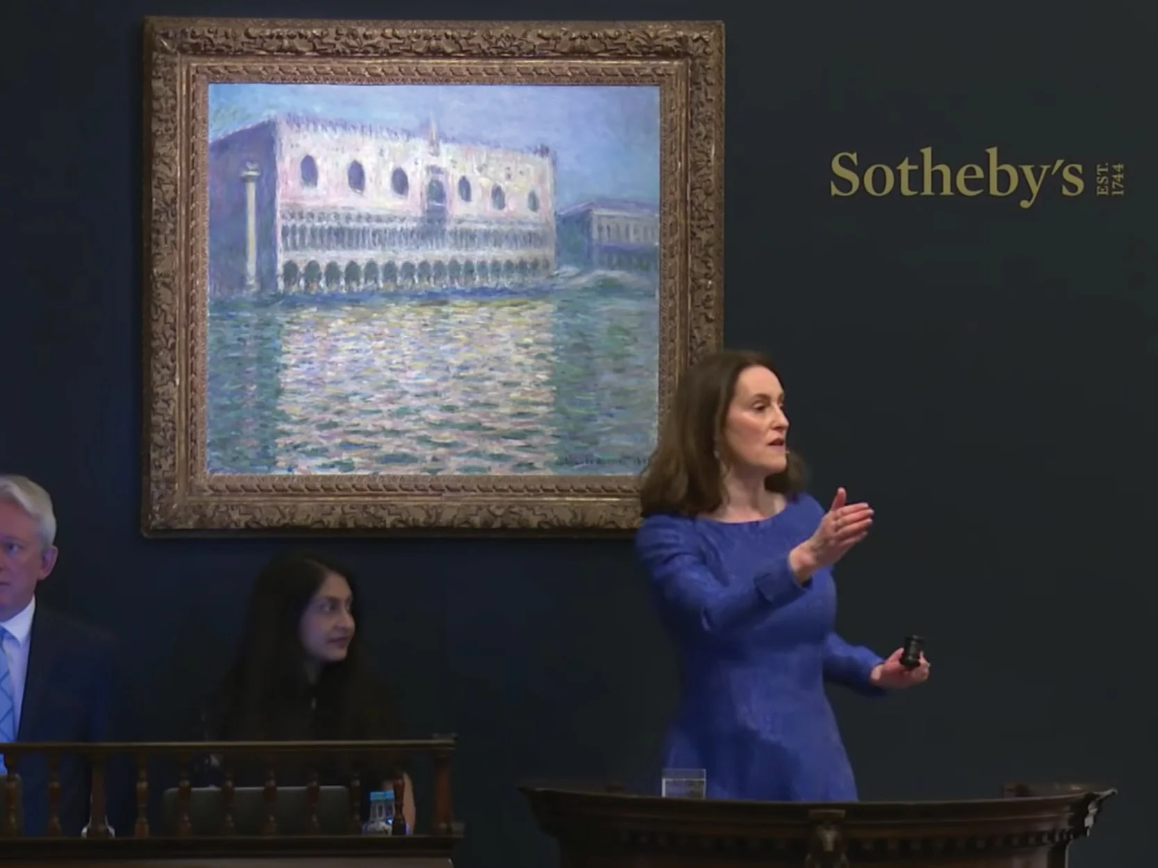 A woman in a blue dress speaks at a Sotheby's auction