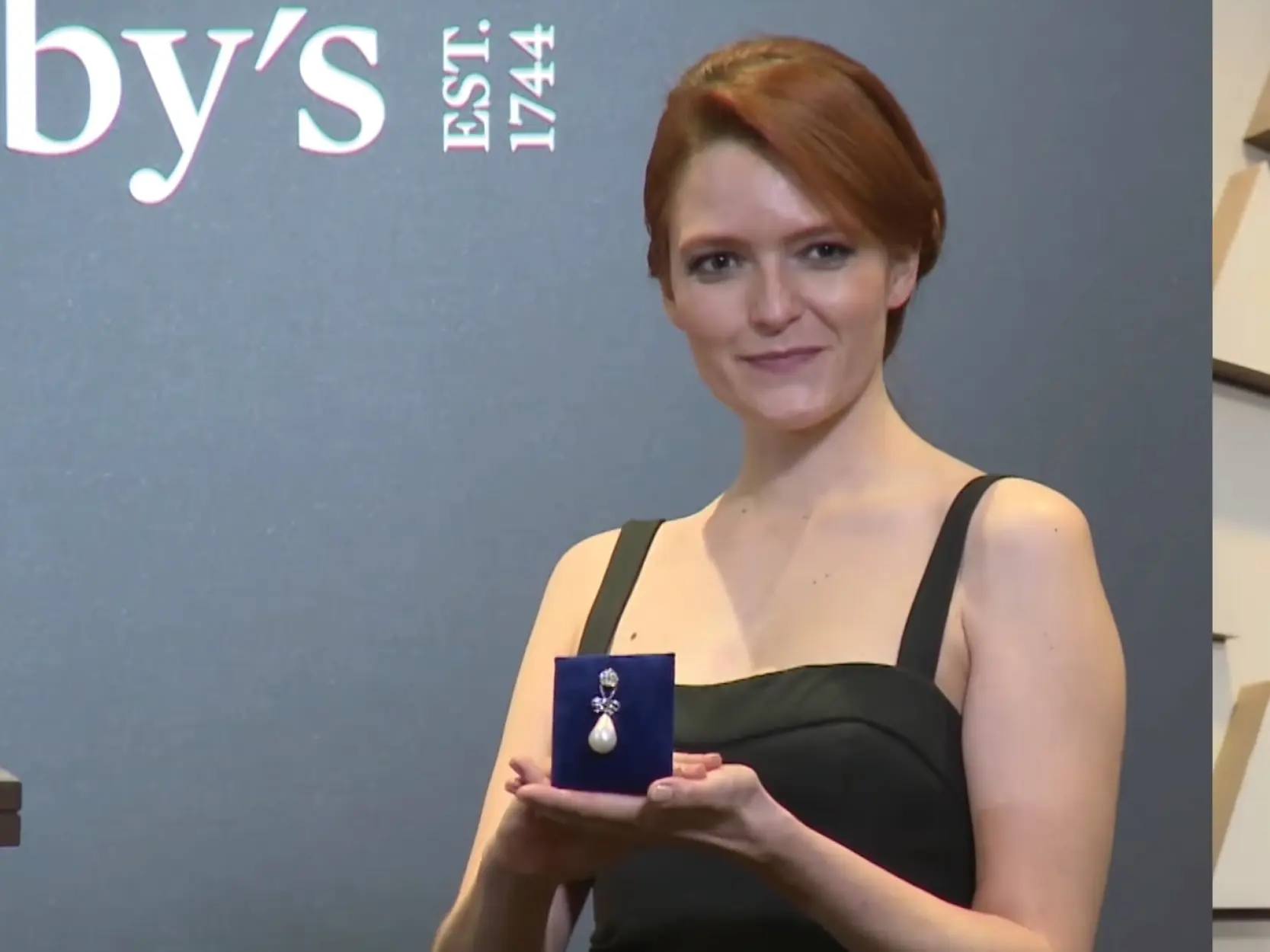 A woman holds up a pearl pendant on blue velvet