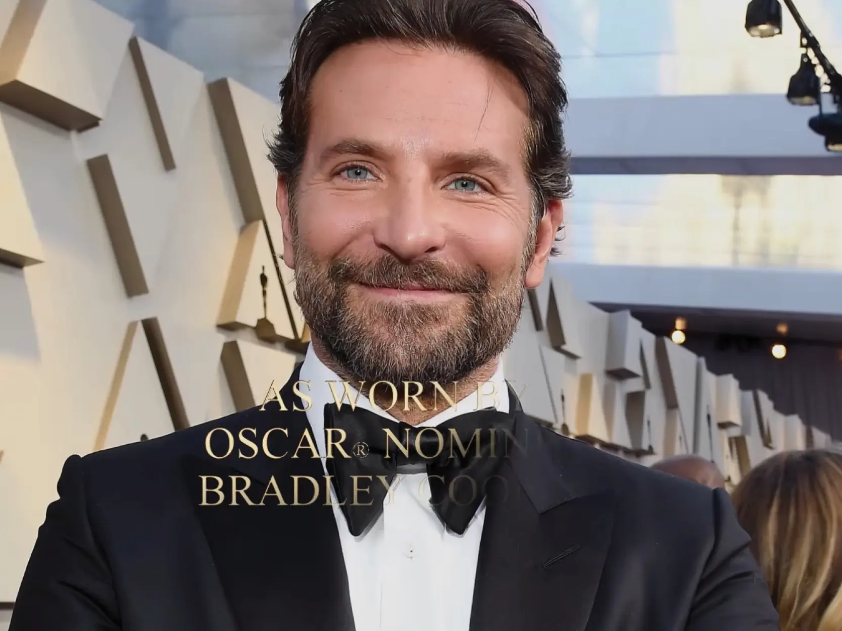 A smiling Bradley Cooper in a tuxedo at an event.