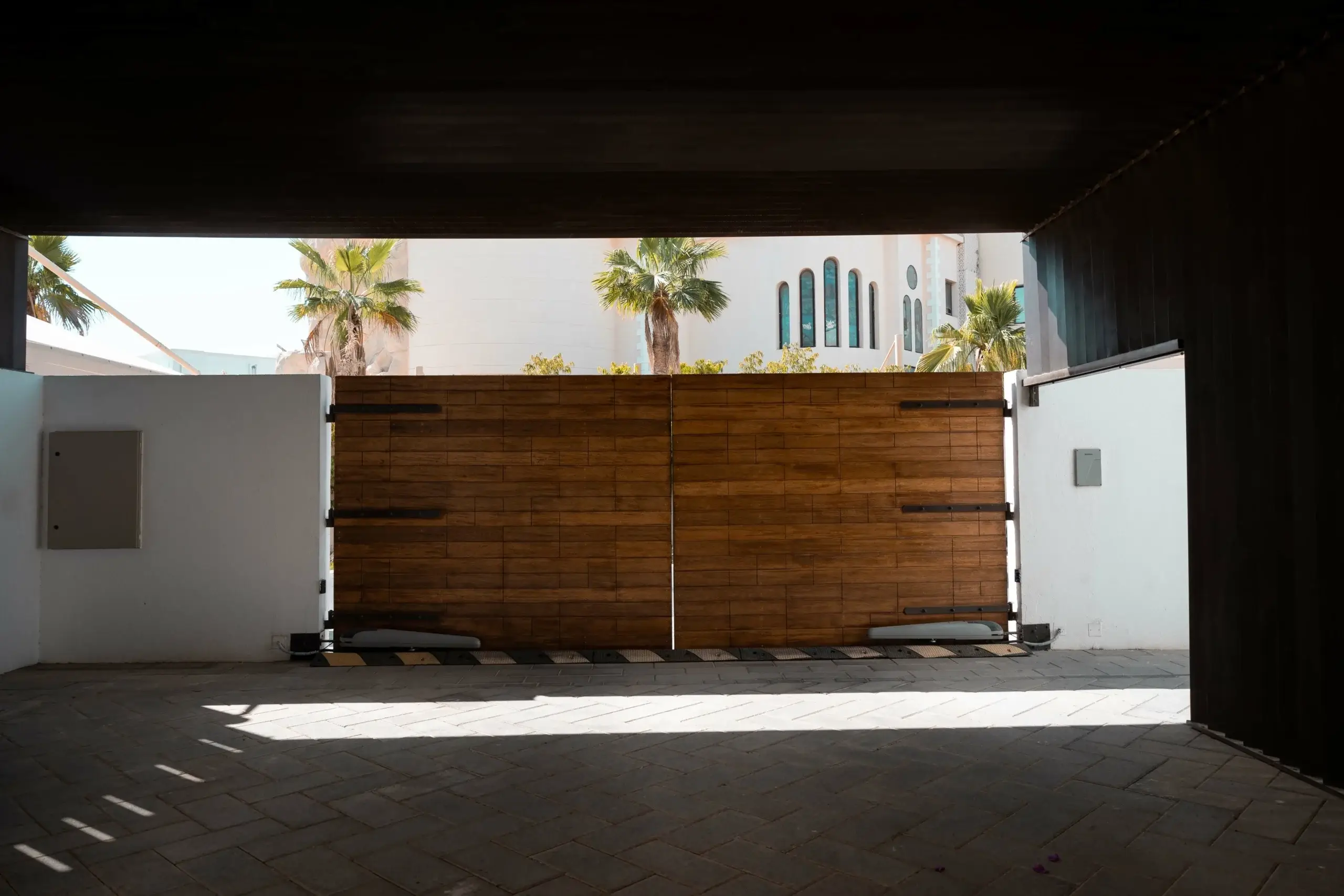 Wooden entrance gate with palm trees and building.