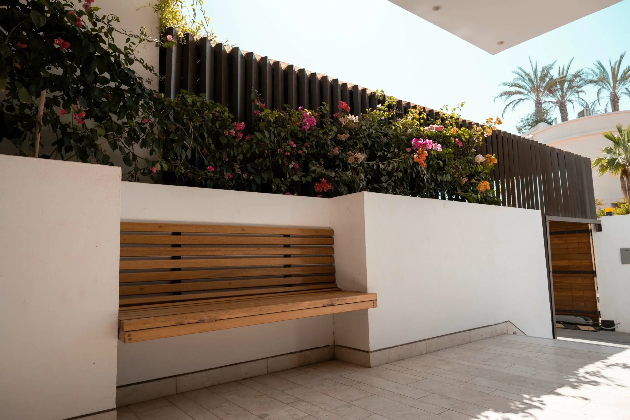 Outdoor patio with wooden bench and flowering plants.