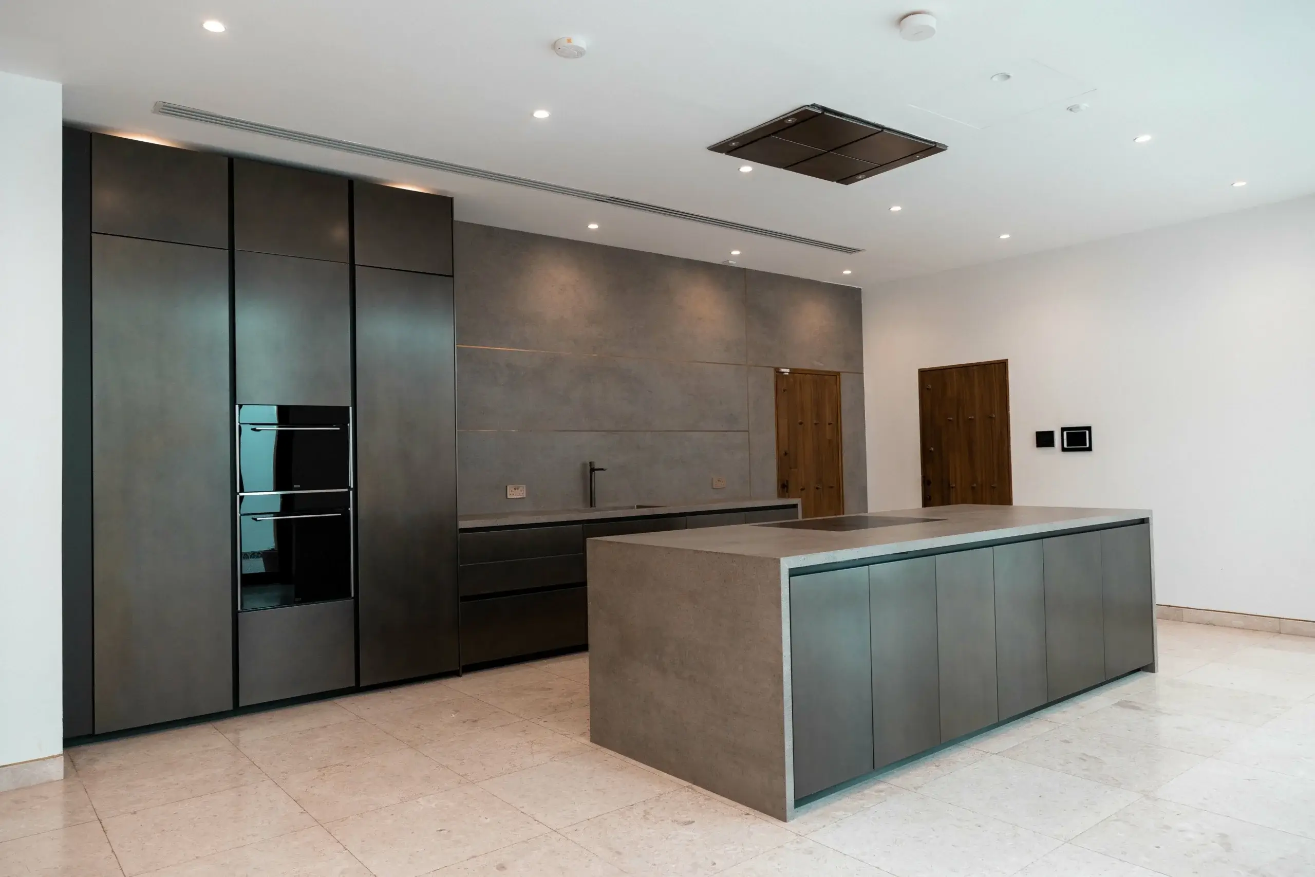 Modern kitchen with island, dark cabinets, ovens.