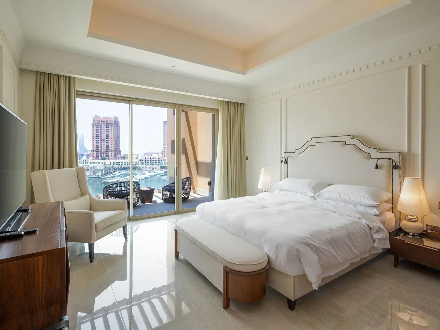 A bedroom with a bed, armchair, and balcony with a view