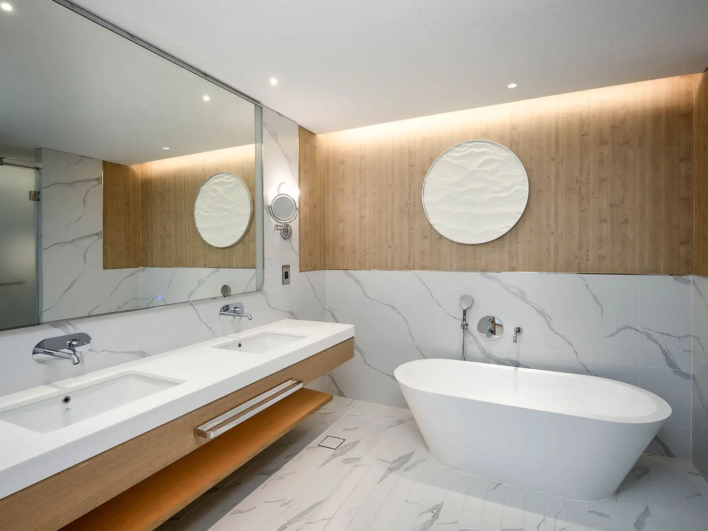 Modern bathroom with tub, dual sinks, marble, wood.