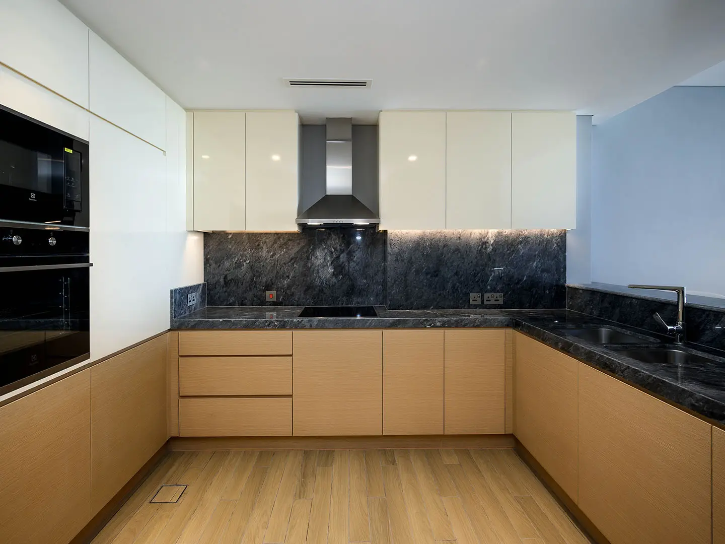 Sleek kitchen with light wood, dark marble, appliances.