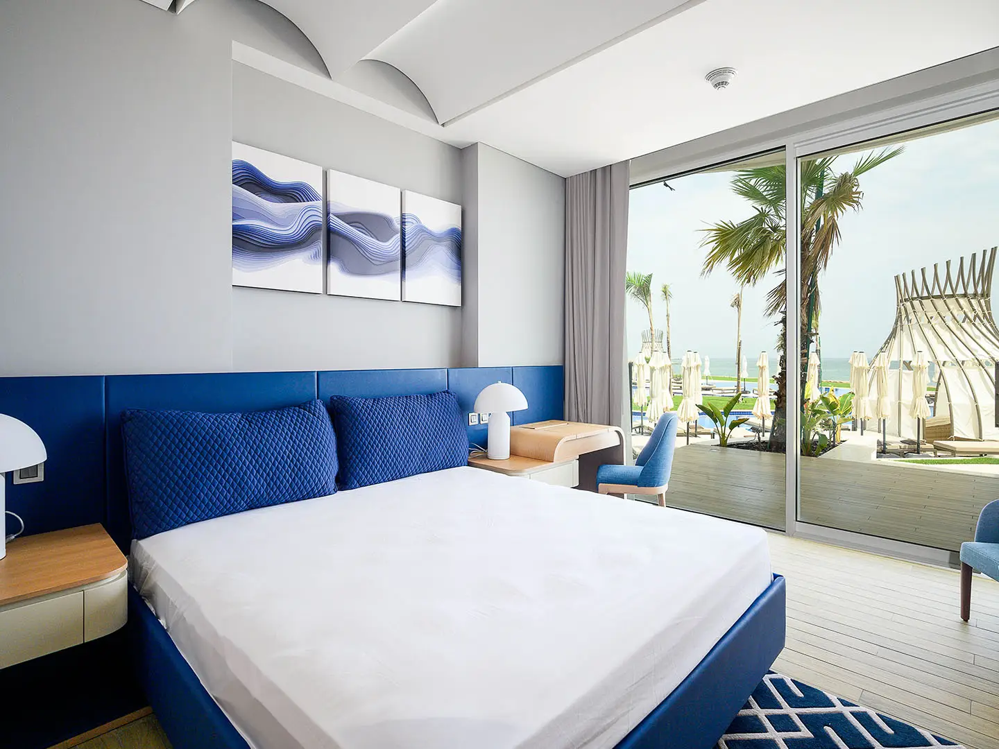 A bright bedroom with a blue bed and balcony view.