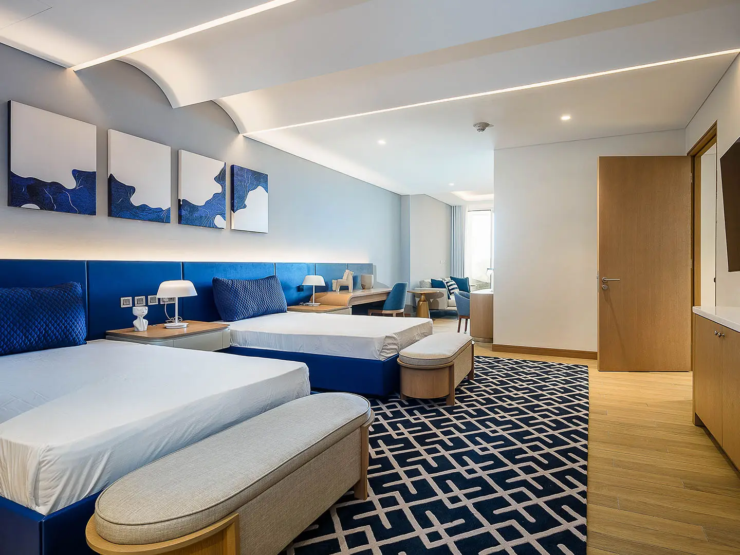 A spacious hotel suite with two beds and a desk area