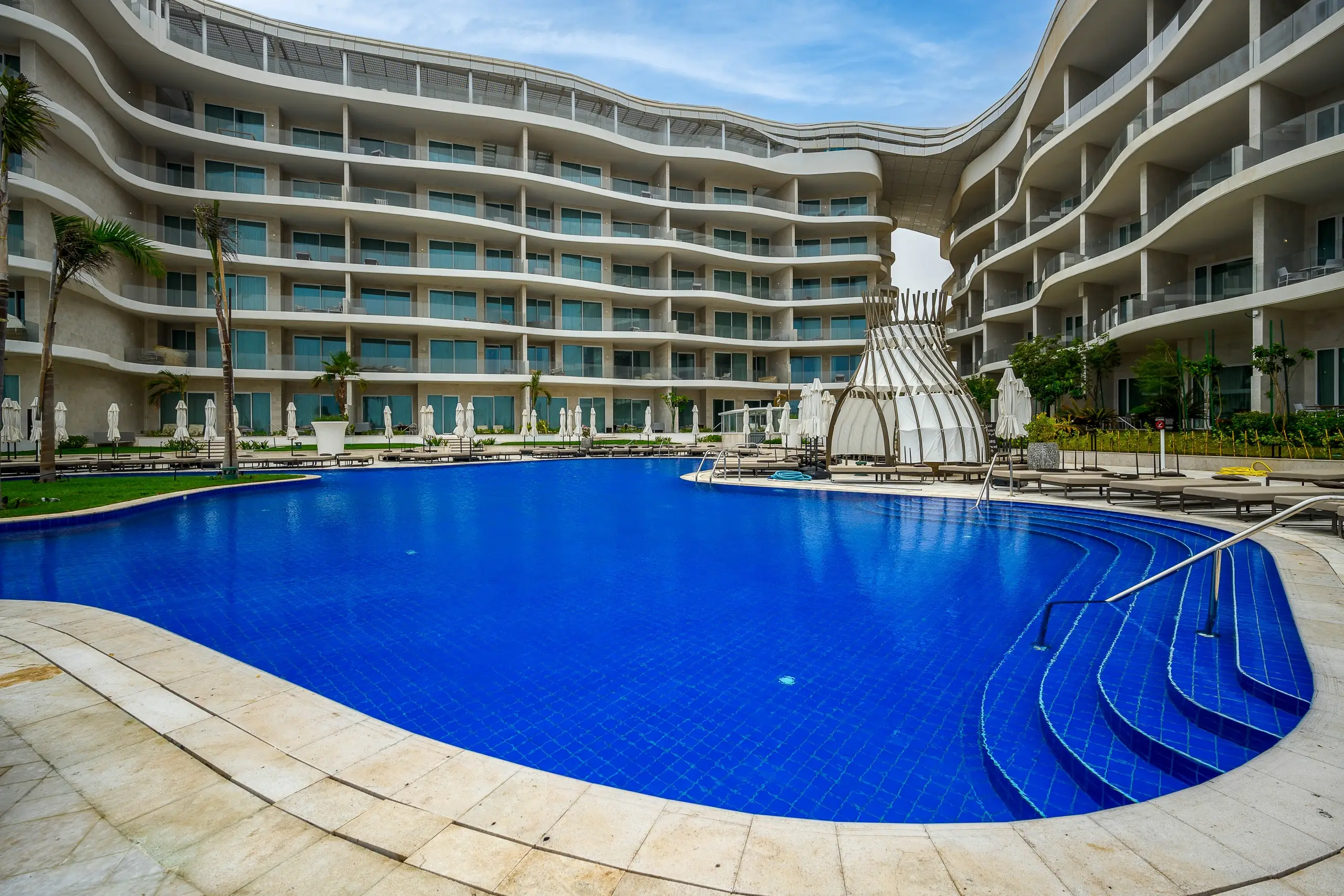A curved hotel with a large blue pool.