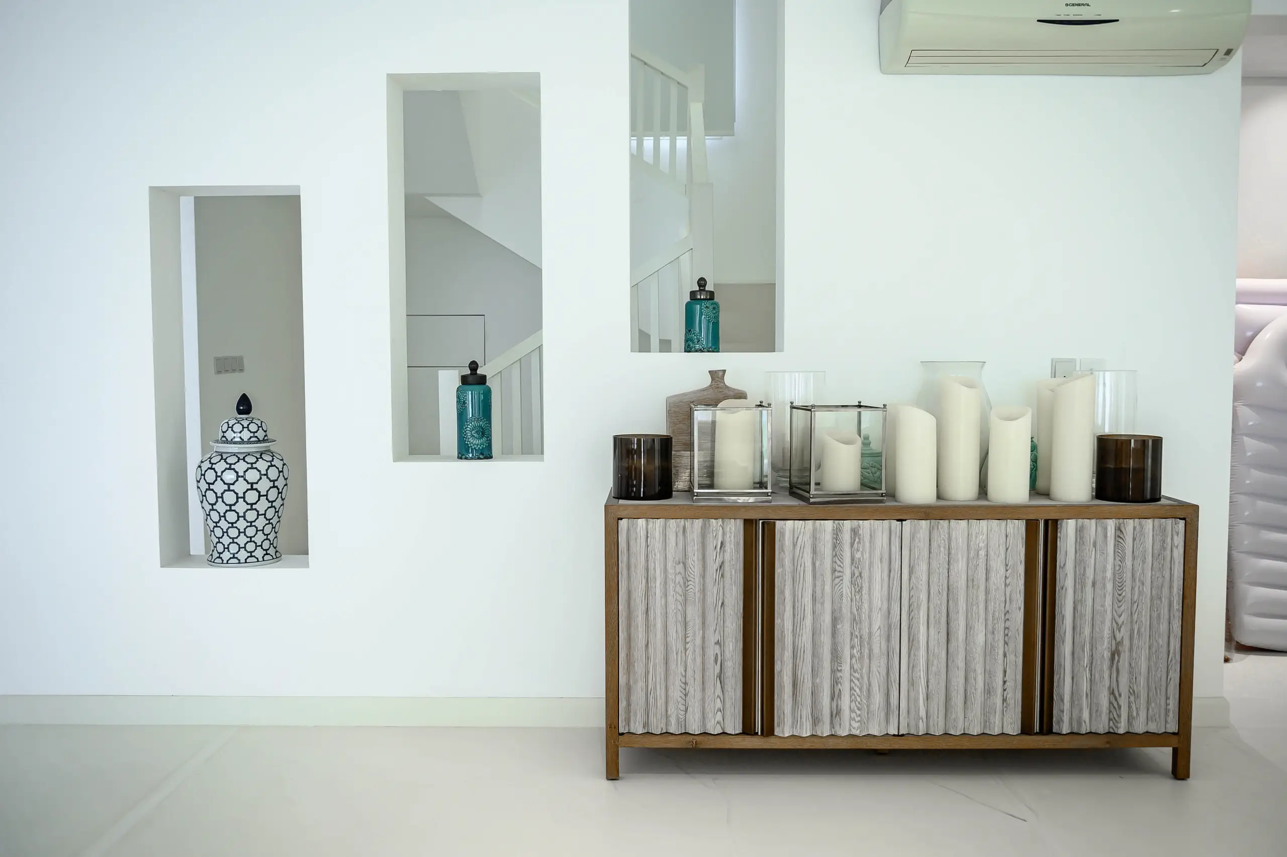 A cabinet with candles in a white room.