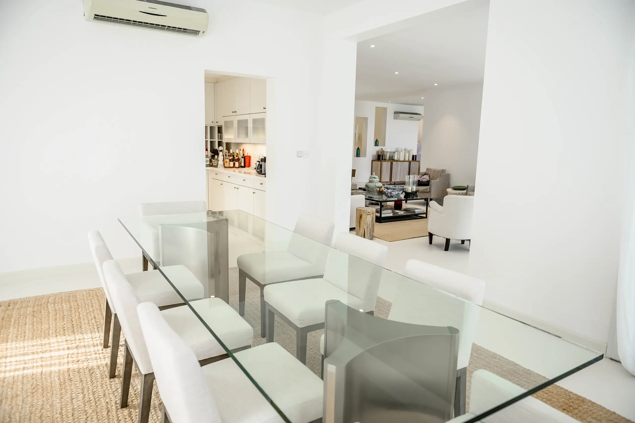 A dining room with a glass table and view into the living room